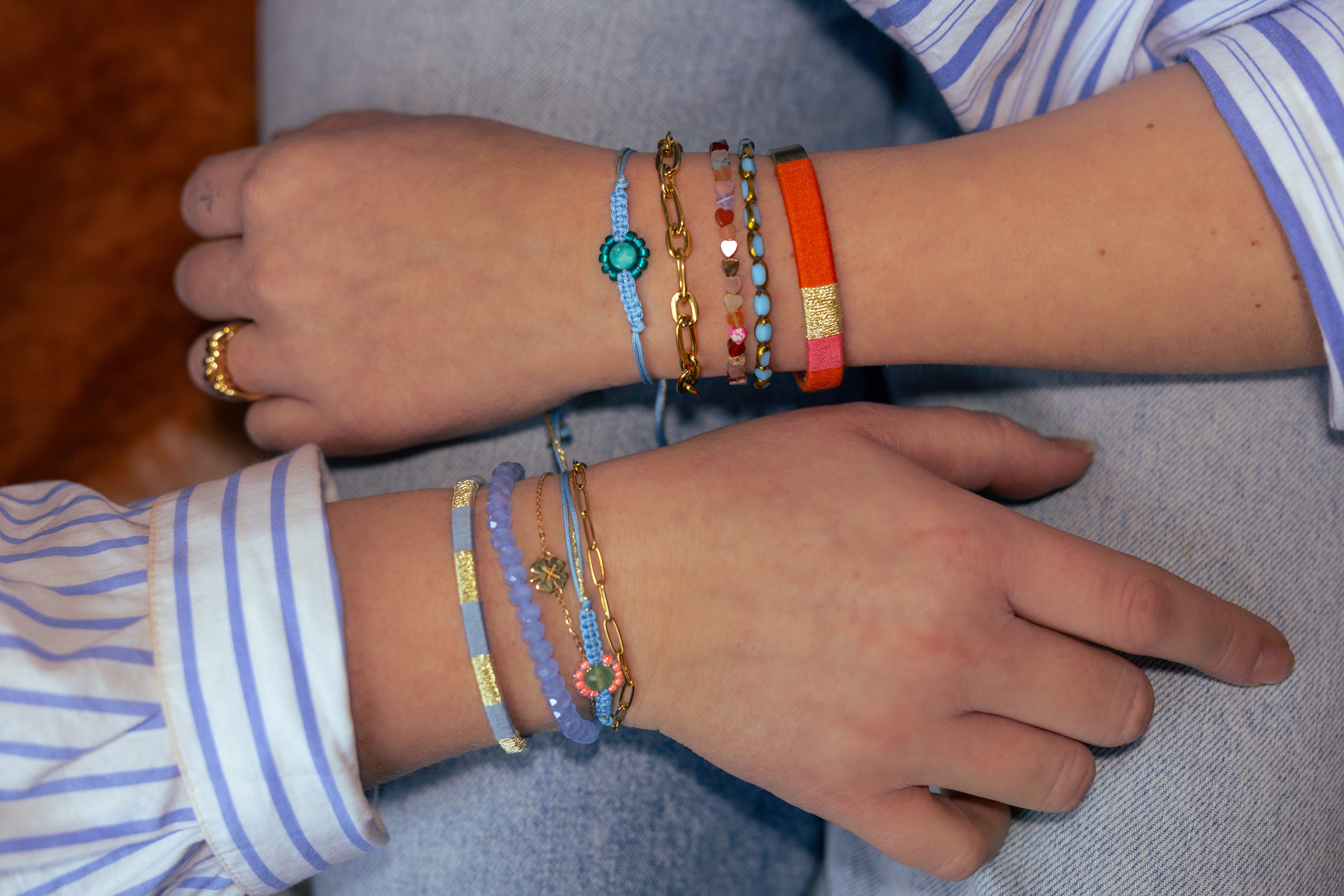 Foto met 2 handen met armbandensets van bert sieraden met blauw en oranje en een hartjesarmband van edelsteen.