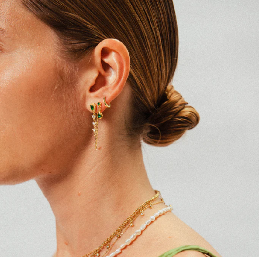 Je ziet oorbellen van Bobby Rose Jewelry in een oor. Het zijn meerdere oorbellen van swarovski en goud.